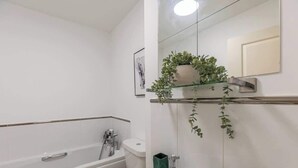Uma casa de banho moderna com uma banheira, uma pia e uma sanita. Há uma planta verde numa prateleira sobre a pia.