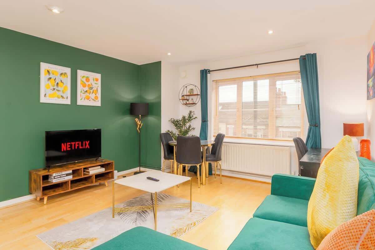 A living room with a TV, green walls, a dining area, and a large window with curtains.