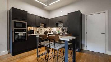 A modern kitchen with dark cabinetry, a built-in oven, and a dining area with bar stools.