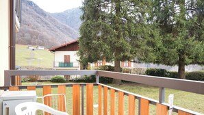 Ein Balkon mit Holzgeländer, einem weißen Kunststoffstuhl und Blick auf einen Berg sowie ein Gebäude mit rotem Dach.