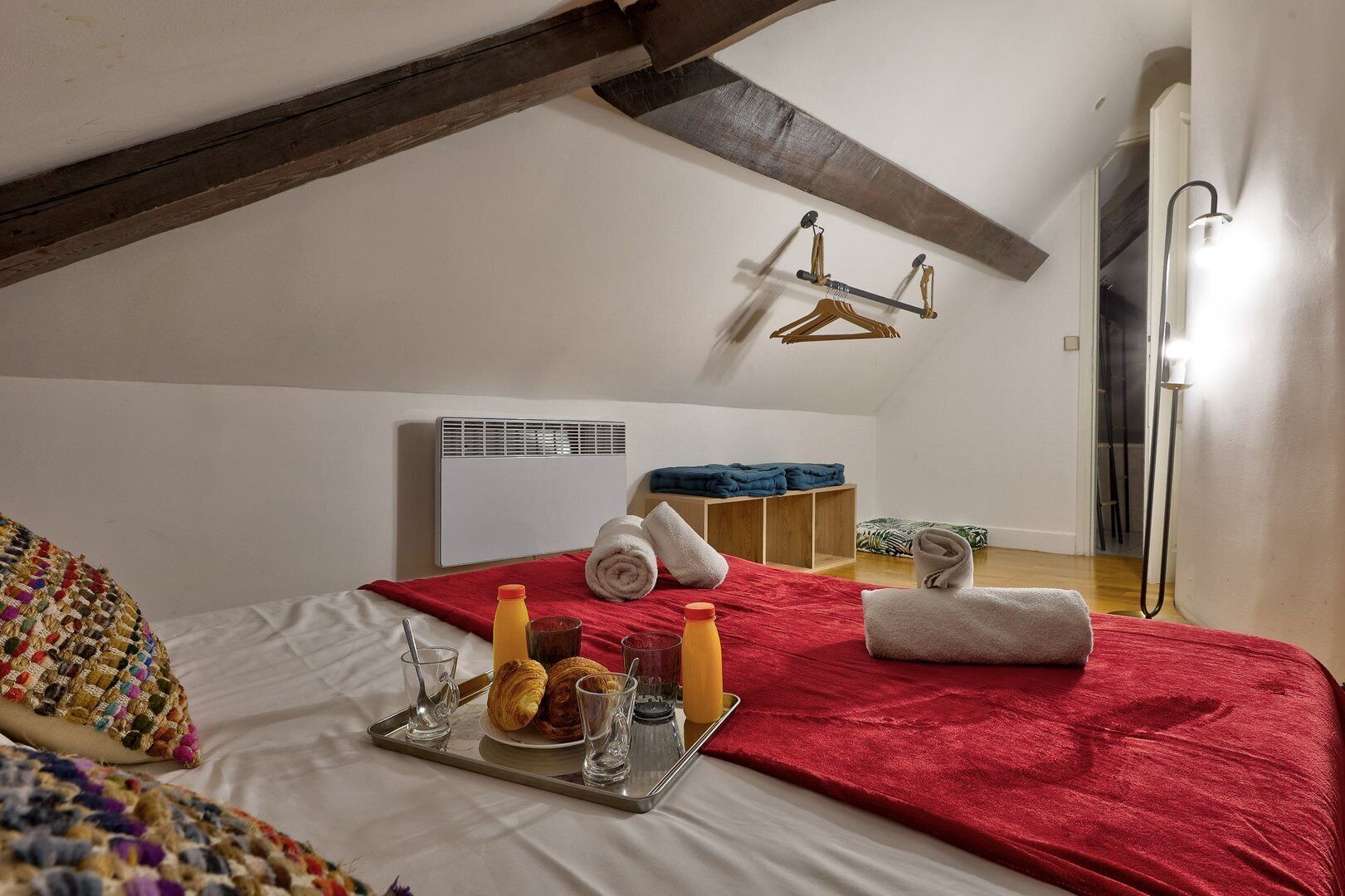 Een gezellige hotelkamer met een bed, een dienblad met ontbijtartikelen, een rode plaid en een handdoekhouder.