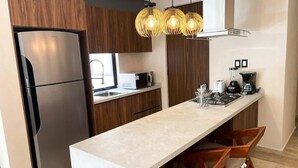 A modern kitchen with a stainless steel refrigerator, wooden cabinets, a marble countertop, and pendant lighting. - Golf Course Condo with Pool & Beach Access (Puerto Aventuras)