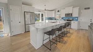 Eine moderne Küche mit weißen Schränken, einer großen Kochinsel mit Barhocker, einem eingebauten Backofen und einer Mikrowelle.