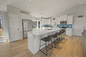 A modern kitchen with white cabinetry, a large island with bar stools, a built-in oven, and a microwave. - Peaceful home with dock, kayaks and sunset views (Deltaville)