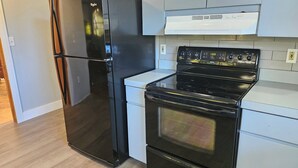 A kitchen with a black refrigerator, a stove, and white cabinets.