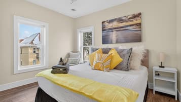 A bedroom with a bed, a window, a painting, and a nightstand.