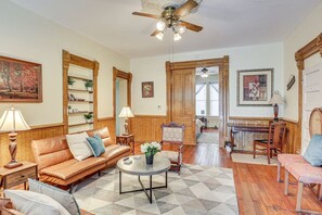 A spacious living room with a leather sofa, a round coffee table, and a wooden chair. There are bookshelves and a ceiling fan.