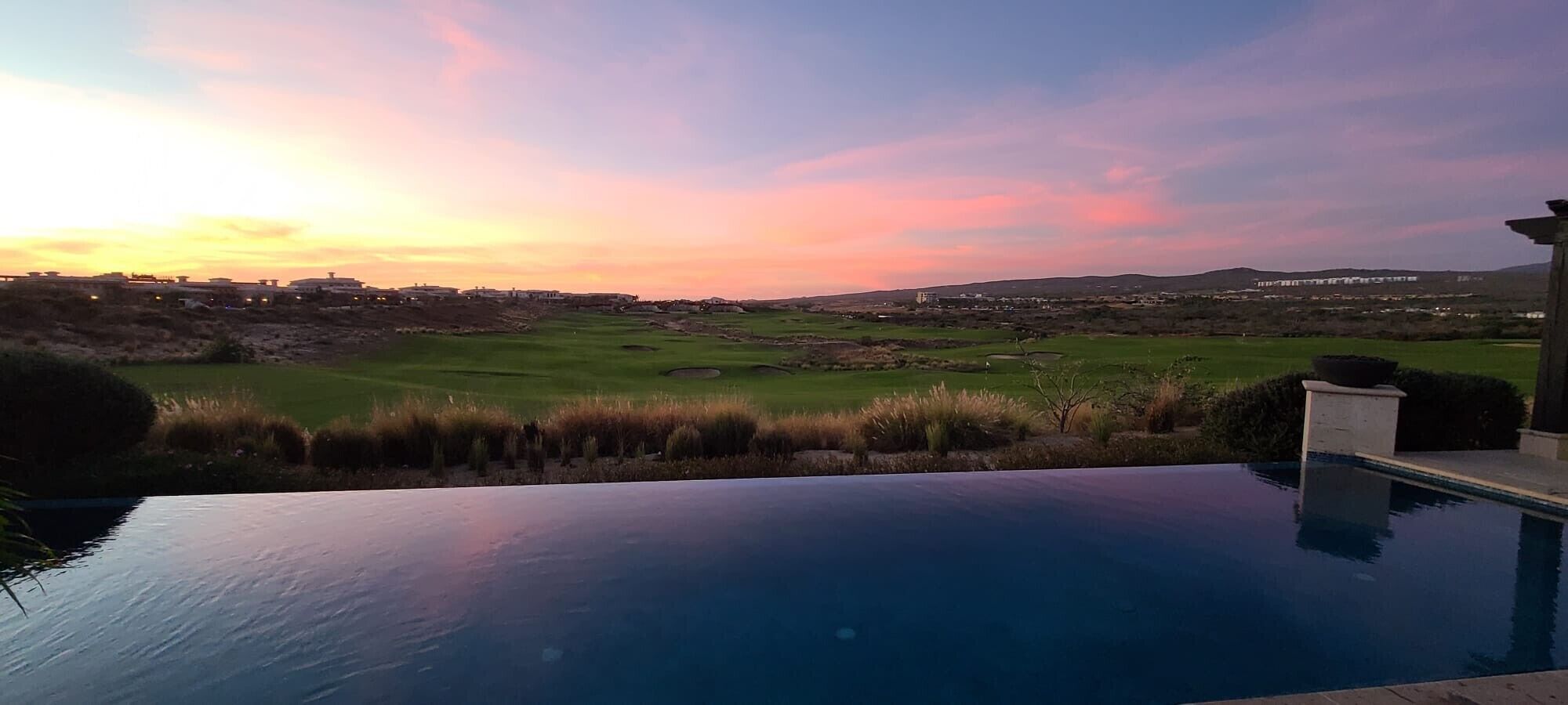 A swimming pool with a view of a golf course and distant hills.