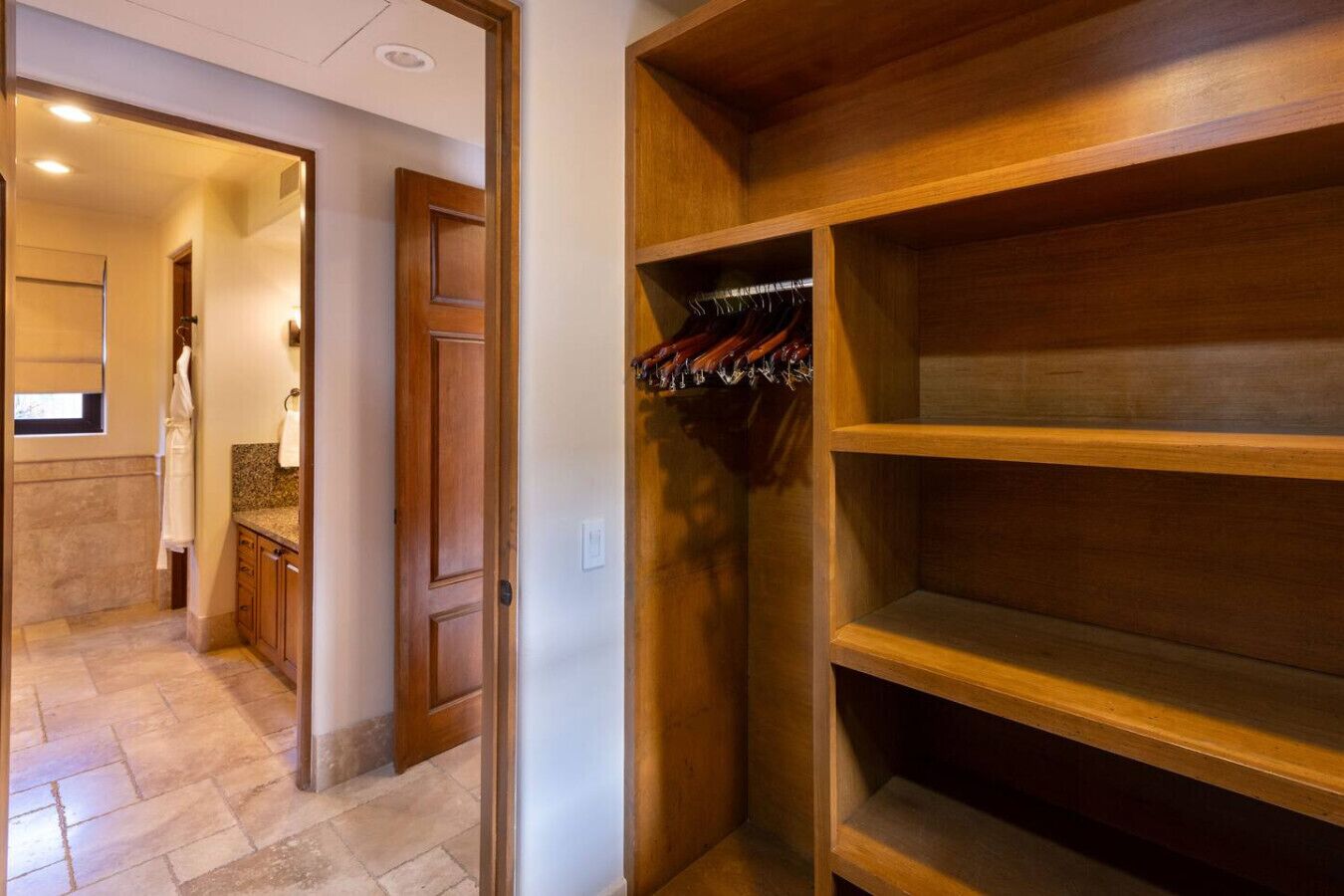 Un couloir menant à une salle de bain avec une porte en bois et un placard doté d’étagères et de penderies.