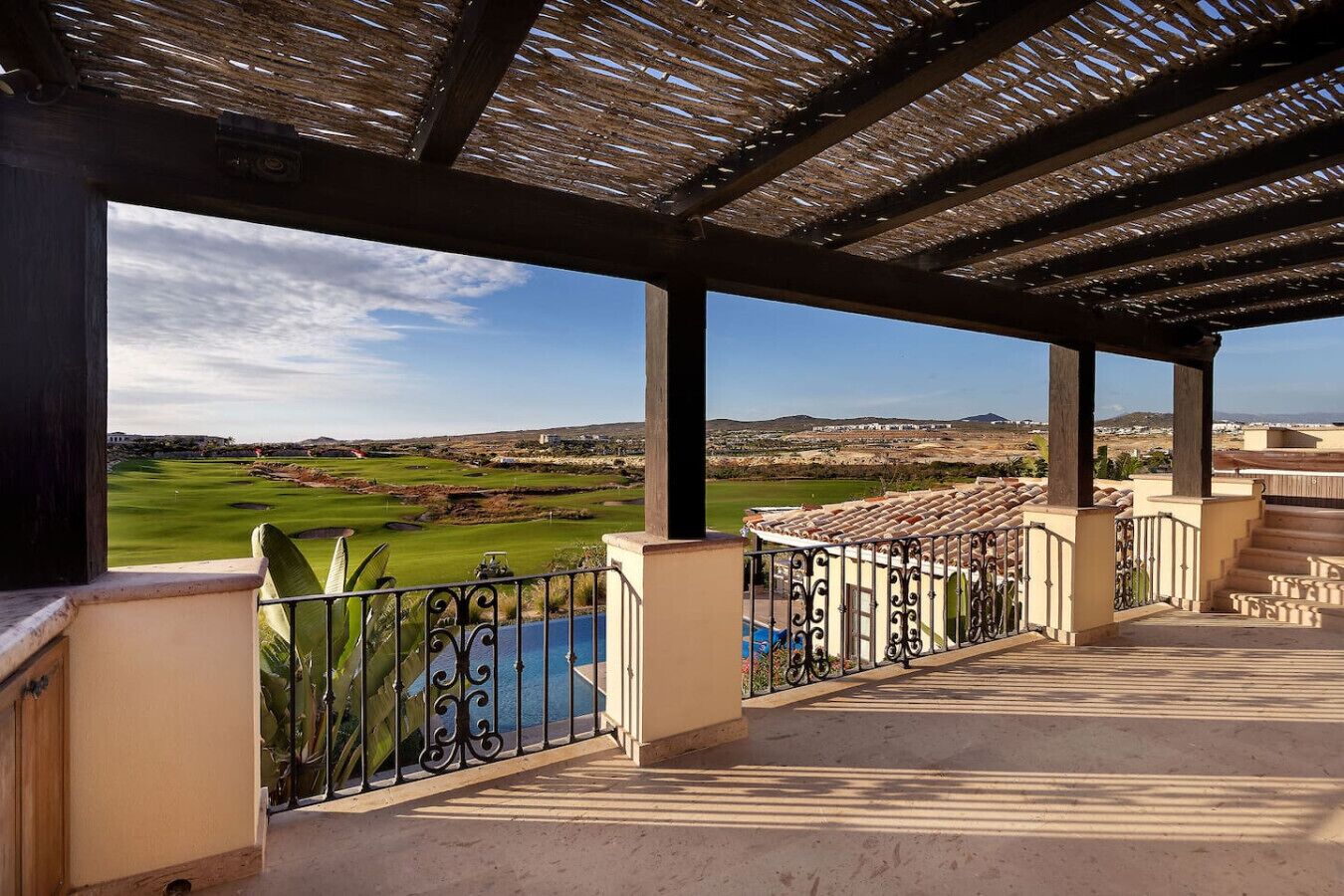 A covered outdoor area with a view of a golf course and a pool.