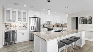 Une cuisine moderne avec des meubles blancs, un îlot en granit, des appareils en acier inoxydable et des luminaires suspendus.