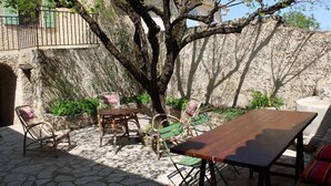 An outdoor patio with stone flooring, wicker furniture, and a wooden table. - Village house Entrechaux (Entrechaux)
