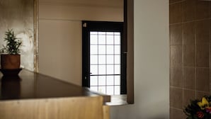 A room with a wooden desk, a potted plant, a tiled wall, and a door with a grid pattern.
