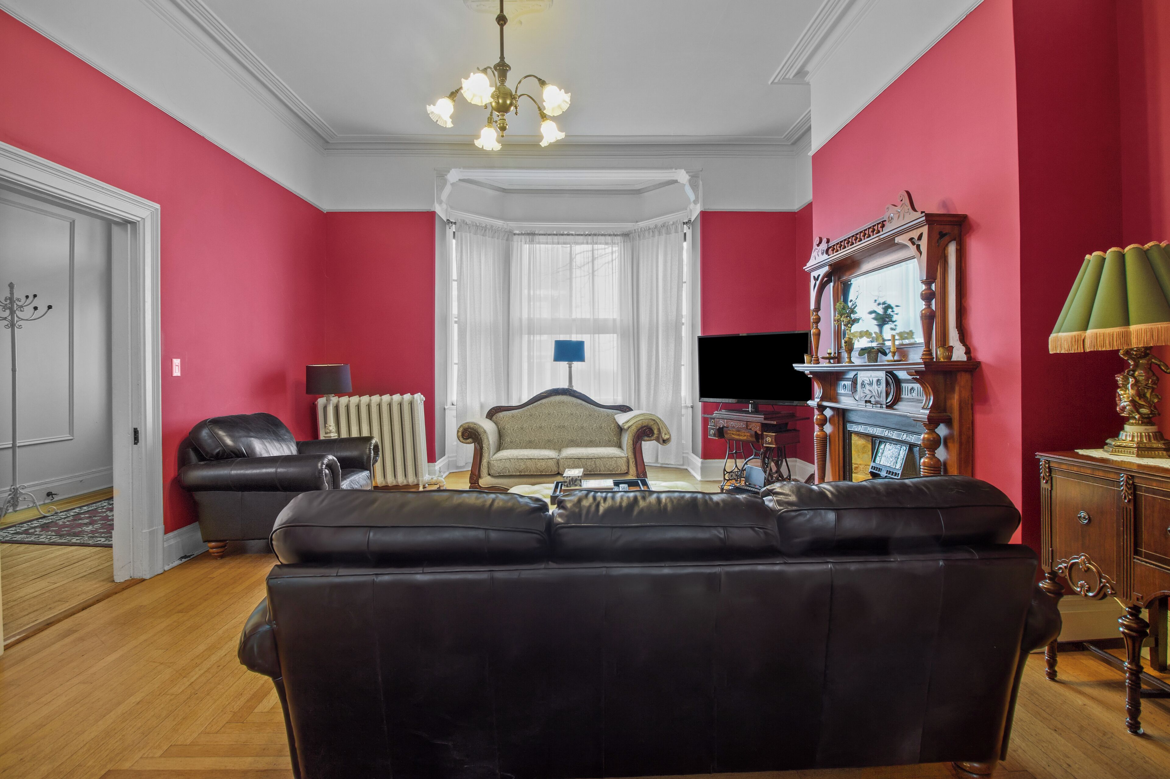 A living room with a black leather sofa, a white-framed armchair, a wooden cabinet with a mirror, and a chandelier.