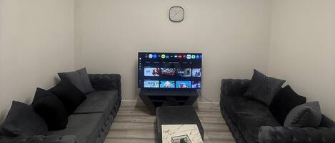 A modern living room with two dark sofas, a flat-screen TV, and a marble coffee table.