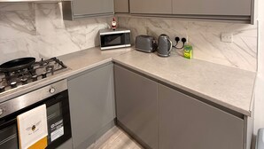 A modern kitchen with grey cabinets, a gas stove, a microwave, a toaster, and a kettle. - Stylish Dream Home With 4 En-suite Bedrooms (Liverpool)