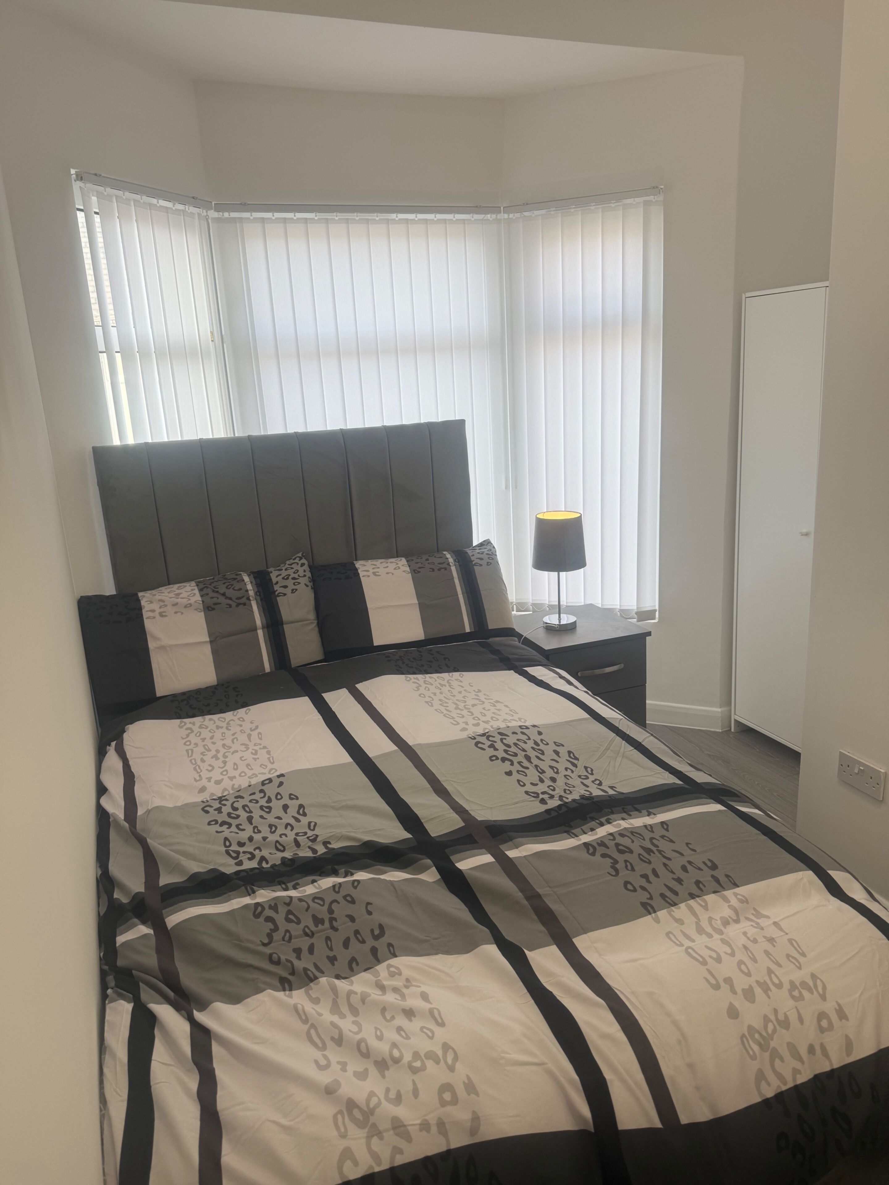 Een slaapkamer met een bed, nachtkastje, lamp en een kledingkast.