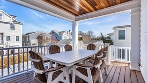Un patio techado al aire libre con mesa y sillas de madera, barandillas blancas y vistas a casas vecinas.