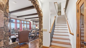 Amplia sala de estar con un arco de piedra, piso de madera y una escalera de madera con barandilla metálica.