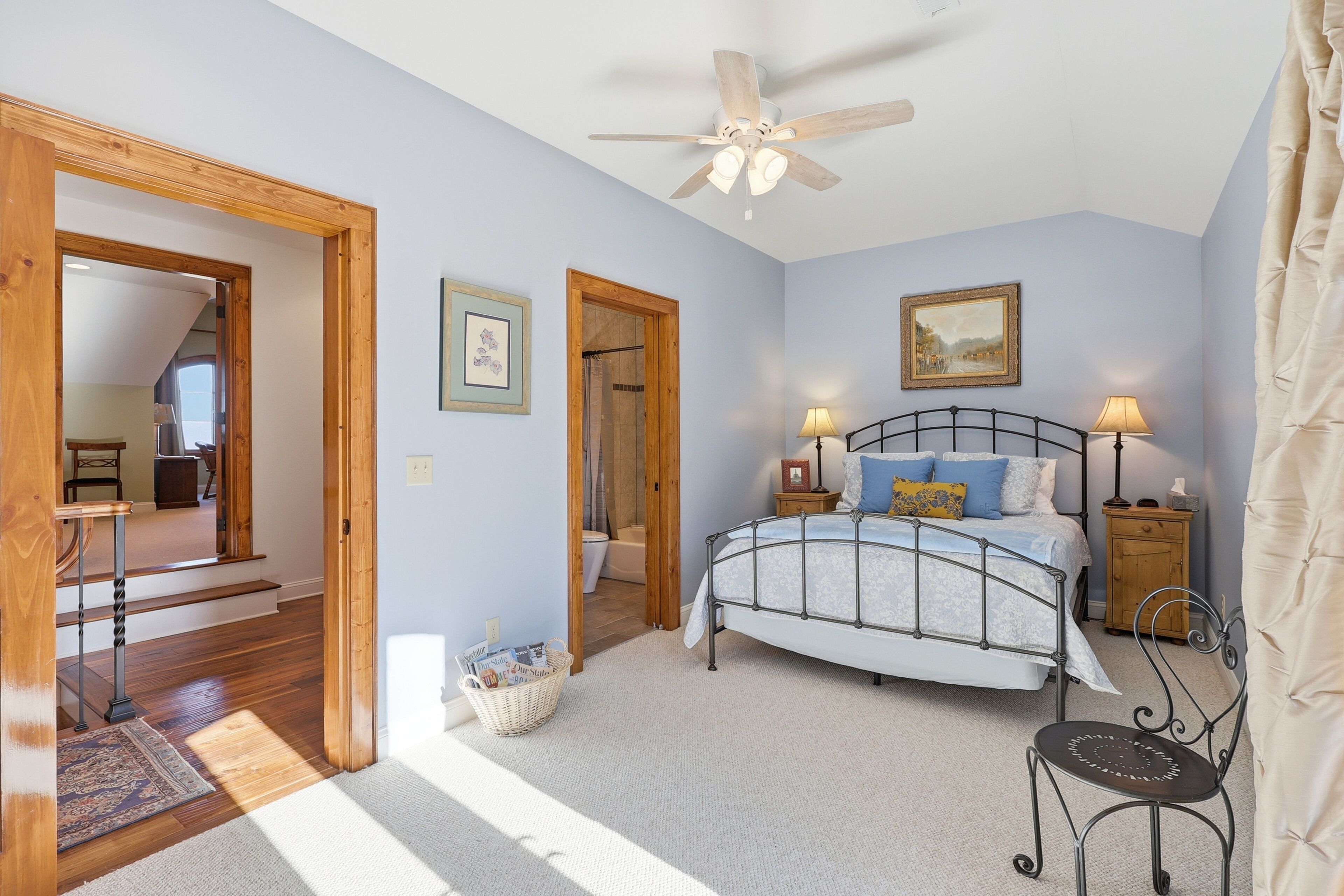 A bedroom with a bed, bedside lamps, a ceiling fan, and a wooden door leading to another room.