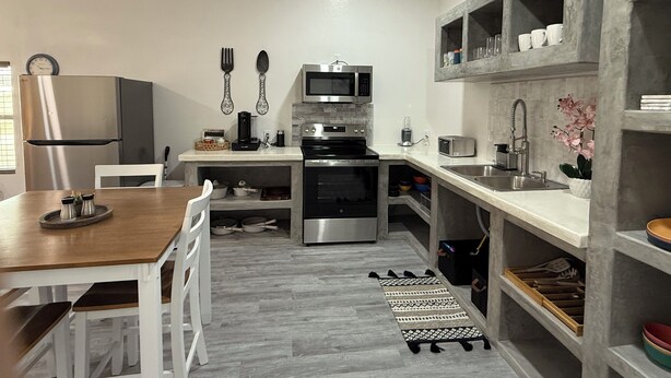 Une cuisine moderne équipée d’appareils électroménagers en acier inoxydable, avec une table à manger en bois et des chaises blanches.