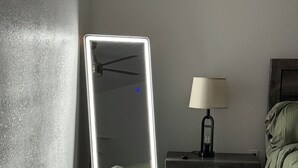 Une chambre à coucher avec un grand miroir, une lampe de chevet, une table de chevet en bois et une couvre-lit verte.
