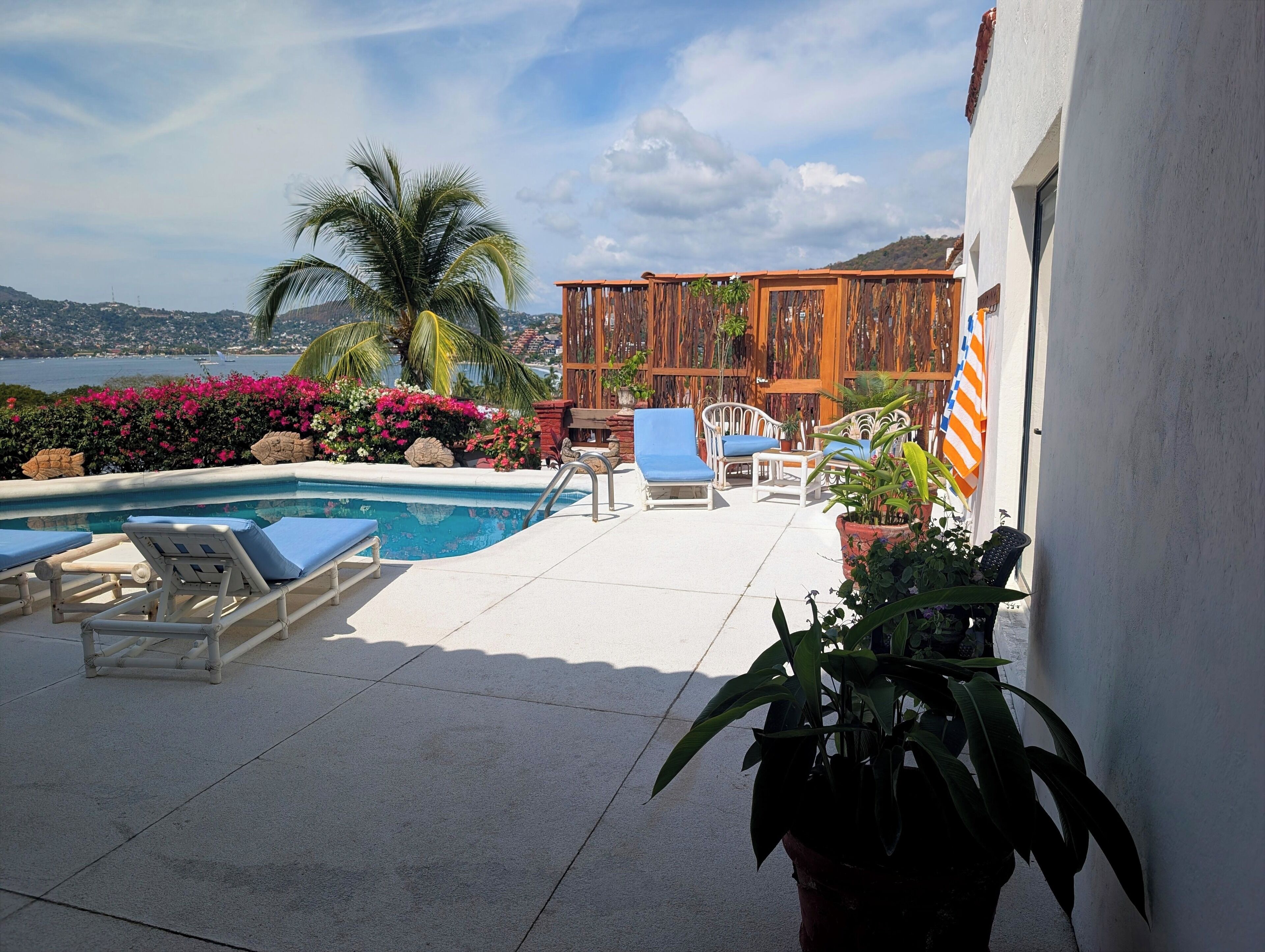 A pool area with lounge chairs, a wooden deck, and a view of the sea.