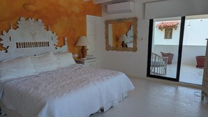 Una camera da letto con un letto grande, un comodino, una lampada, uno specchio e una porta scorrevole in vetro che dà su uno spazio esterno con piante in vaso.