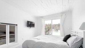 A bedroom with a bed, a TV, a window with curtains, and a view of trees outside. - Getaway 1 hour from Montreal - perfect for relaxing (Saint-Calixte)