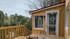A wooden deck with a table and chairs, a glass door, and a view of trees and a body of water. - Getaway 1 hour from Montreal - perfect for relaxing (Saint-Calixte)