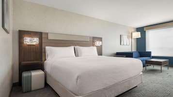 A hotel room with a large bed, a bedside table, a lamp, a sofa, and a window.