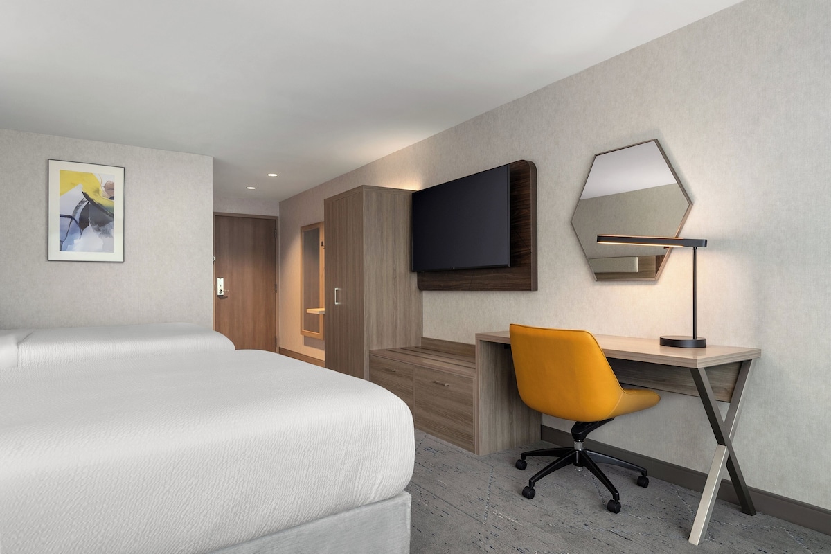 Habitación de hotel con cama, escritorio, silla, televisor y un cuadro en la pared.