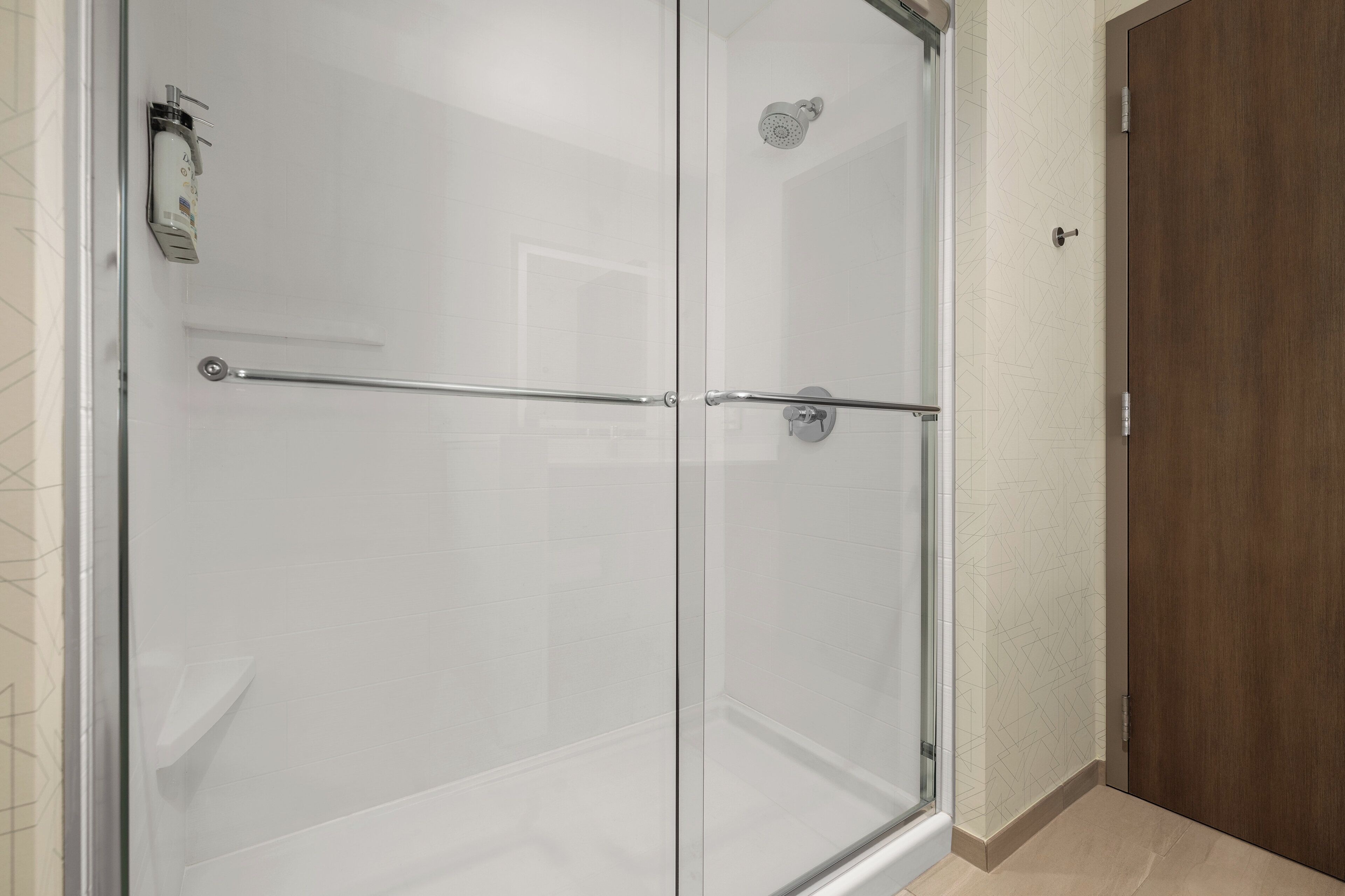 A glass-enclosed shower with a metal handrail, a wooden door, and a tiled wall.