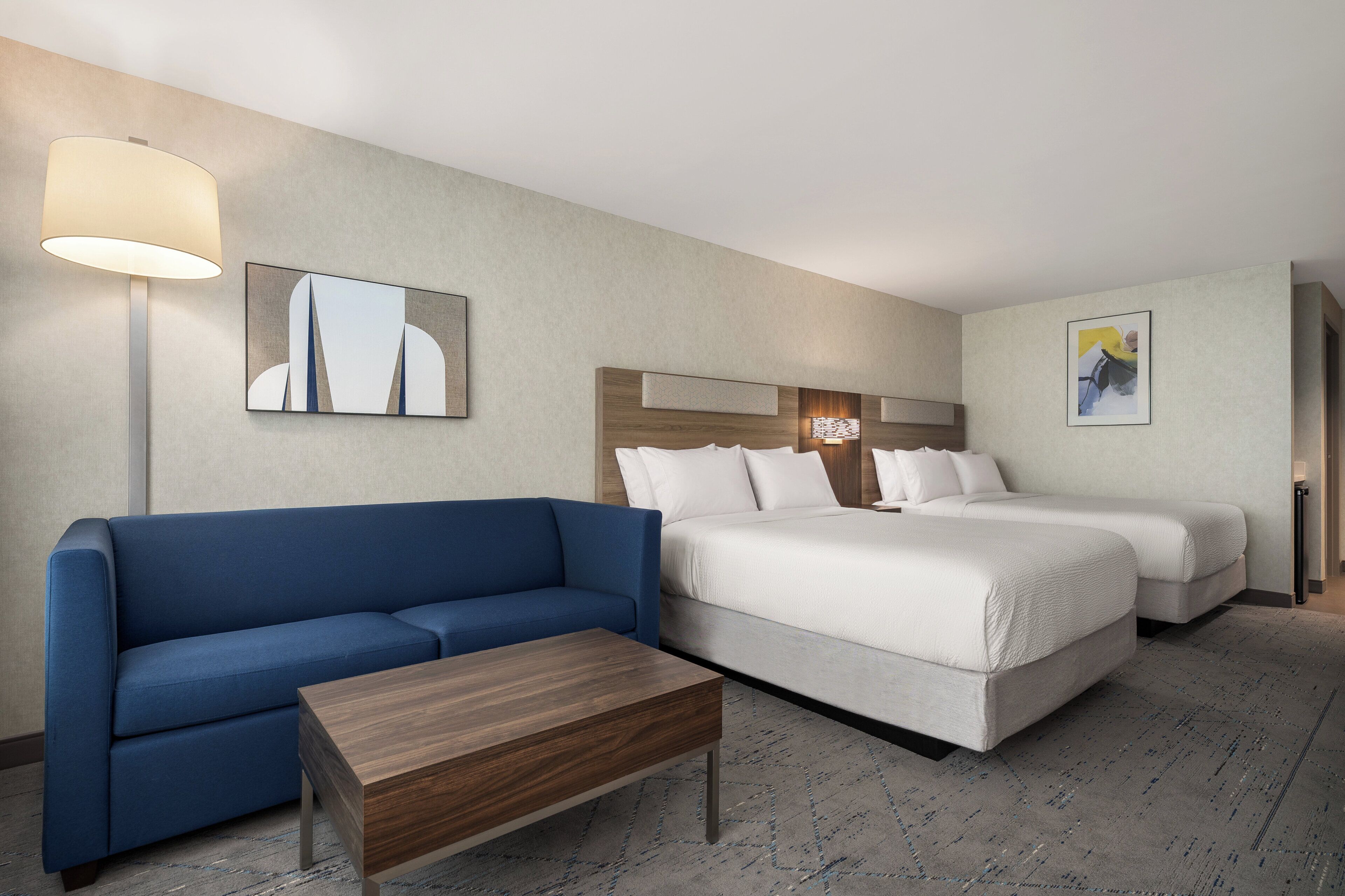 Ein Hotelzimmer mit einem blauen Sofa, einem Holztisch, zwei Betten und einer großen Wandleuchte.