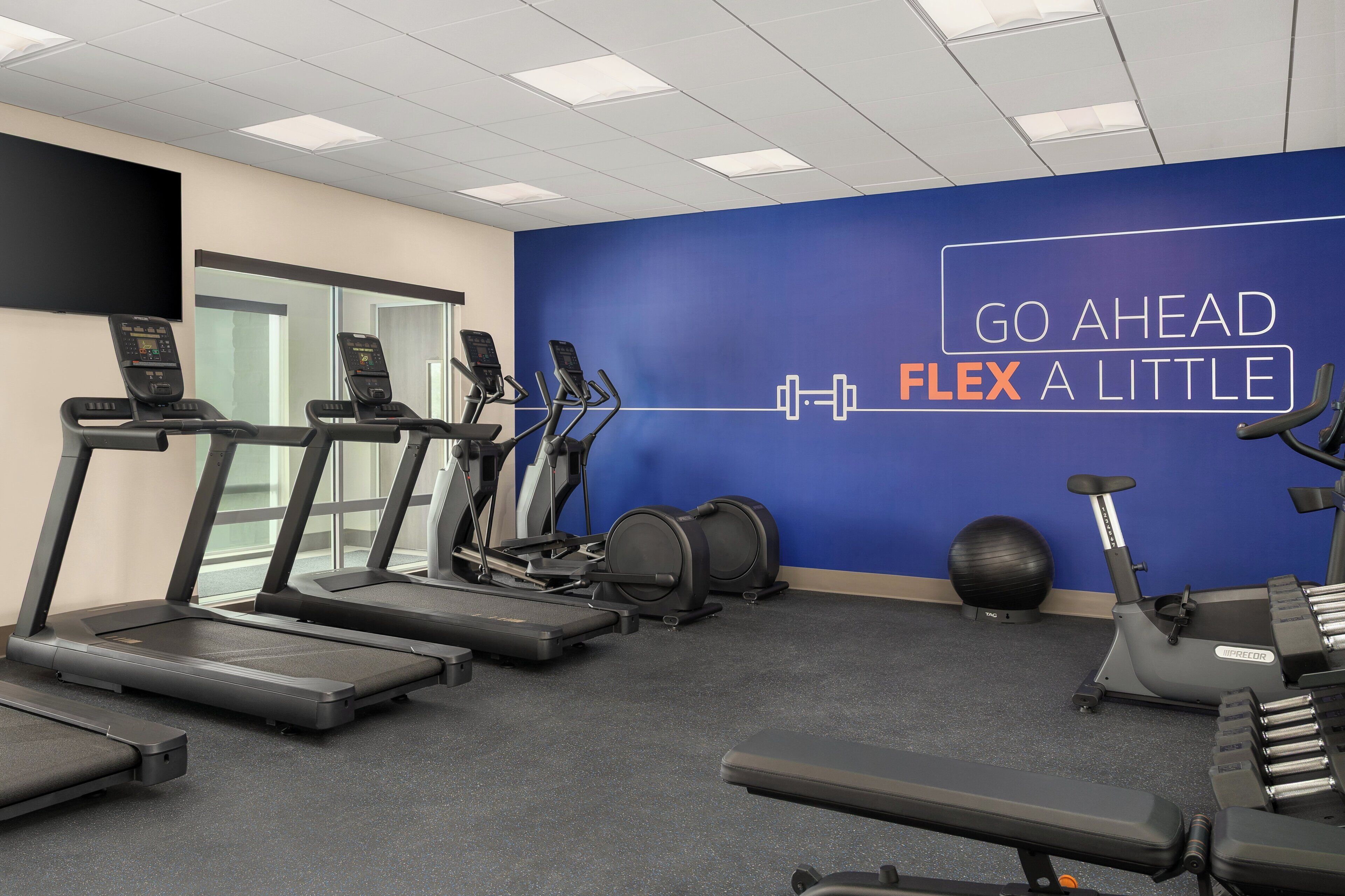 A gym with treadmills, elliptical machines, and a wall with motivational text.