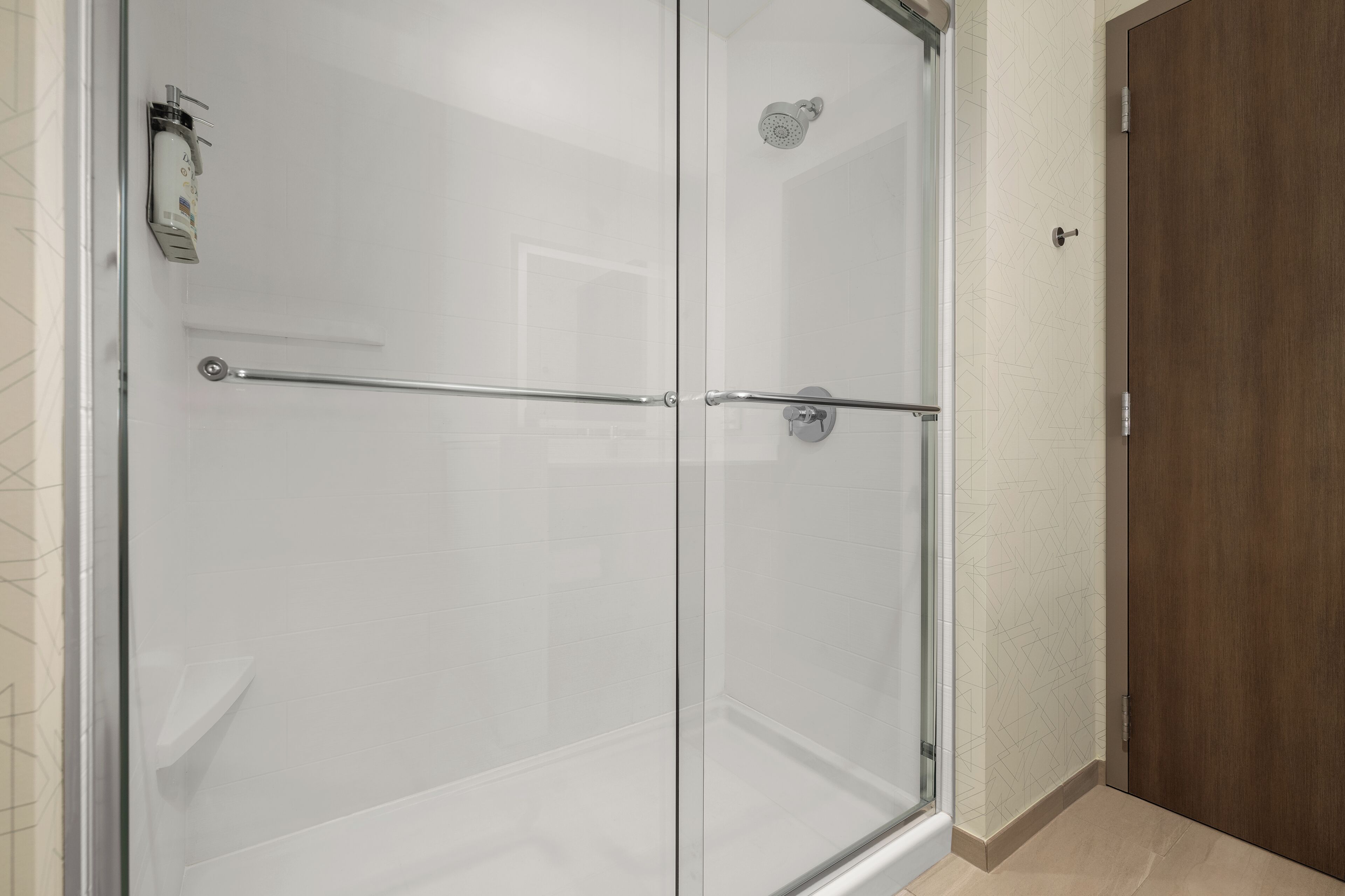 Een douche met glazen wanden, een metalen handgreep, een houten deur en een betegelde muur.