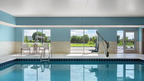 Una piscina con agua azul cristalina, una tumbona y una mesa con sillas.