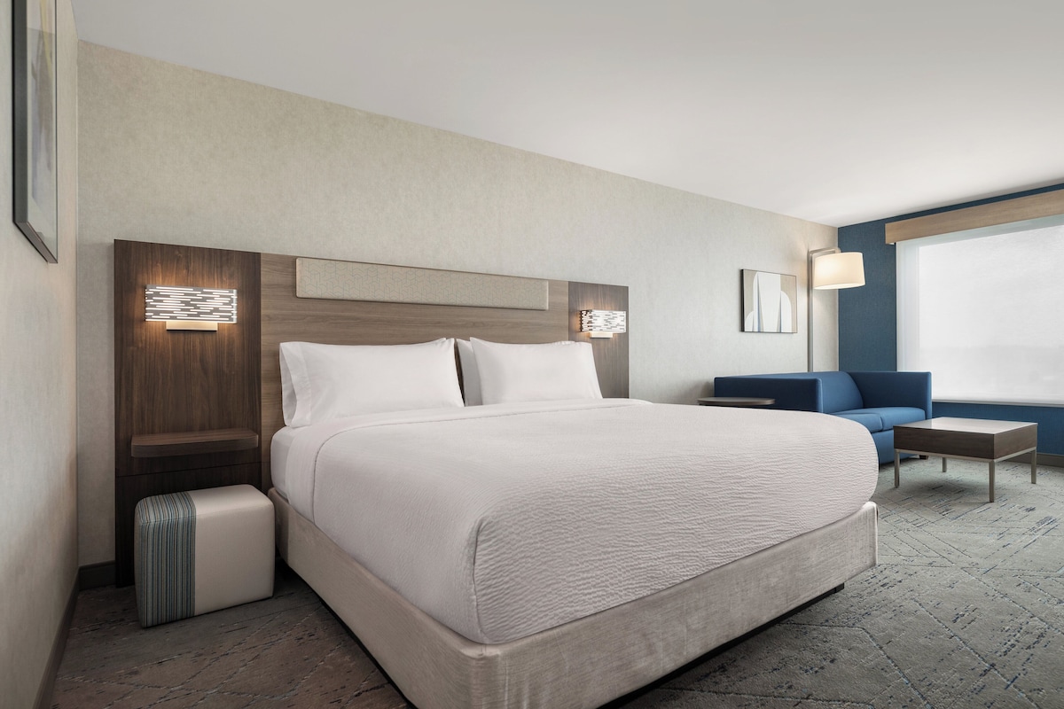 Habitación de hotel con una cama grande, una mesita de noche, una silla, una pequeña mesa y una ventana.