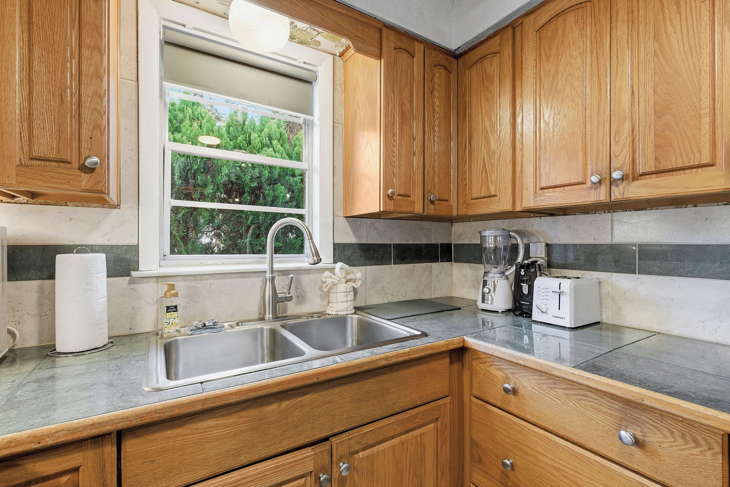 Una cocina con armarios de madera, un lavamanos doble, una ventana y una encimera con un tostador y una licuadora.