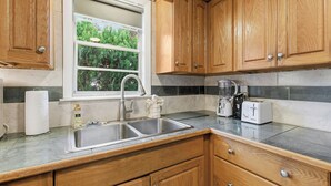Eine Küche mit Holzschränken, einer Spüle, einem Fenster und einer Arbeitsplatte mit Toaster und Mixer.