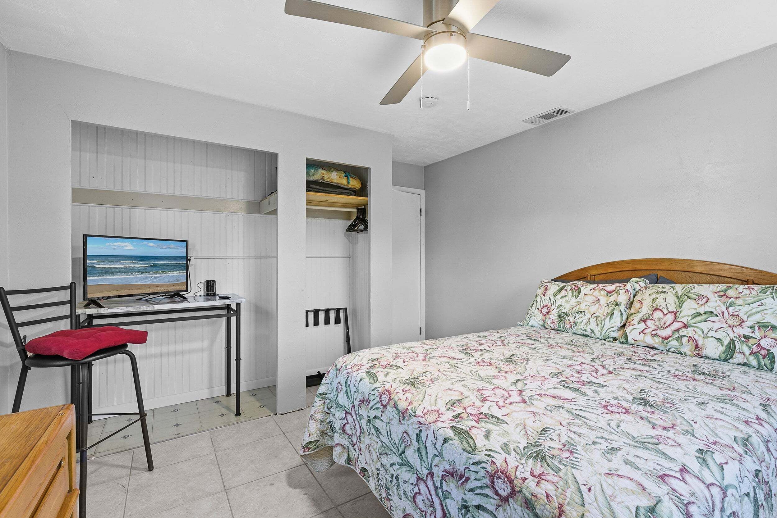 Ein Schlafzimmer mit Bett, Schreibtisch mit Computer, Stuhl und Deckenventilator.