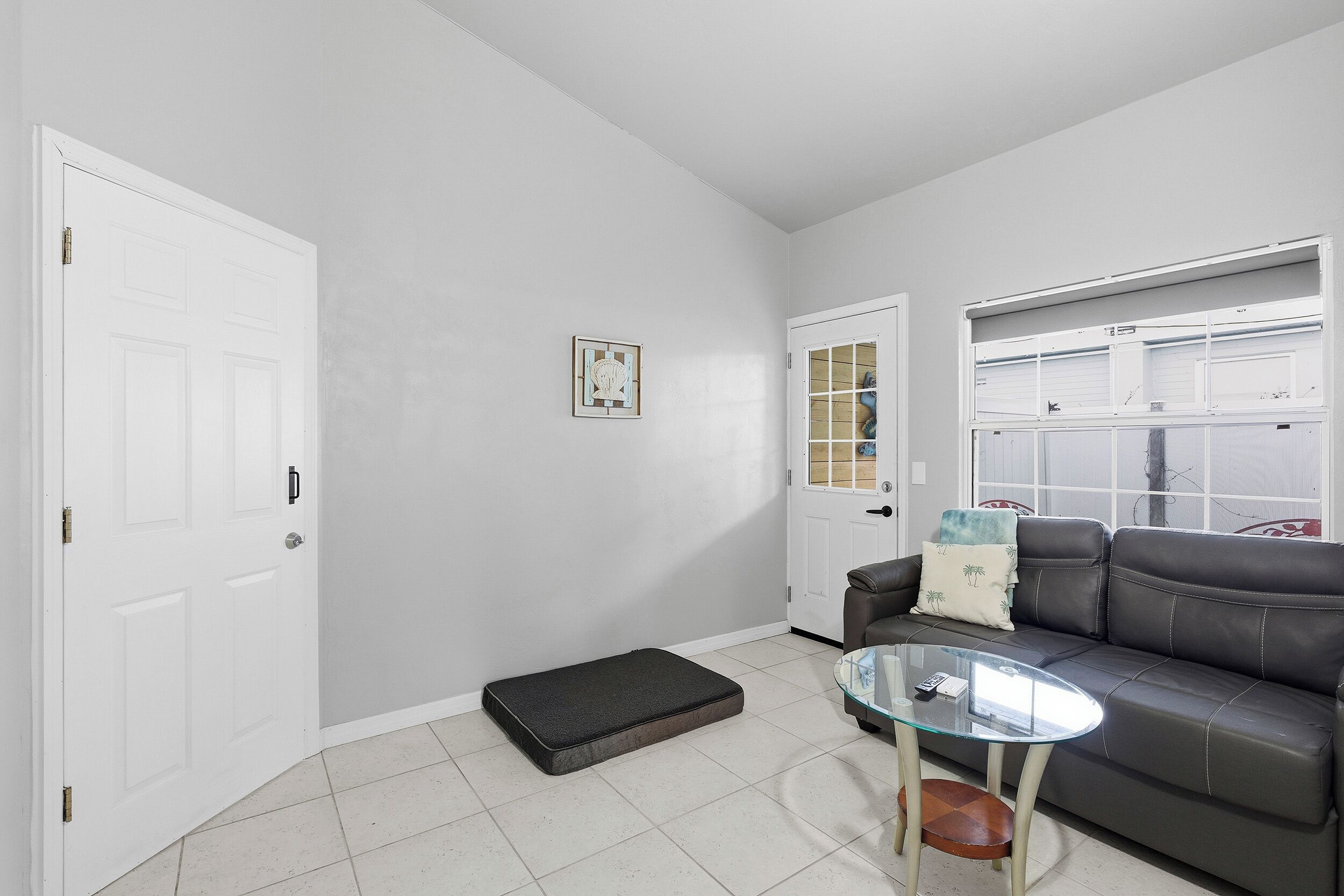 A room with a grey sofa, a glass coffee table, a door, and a small mat on the floor.