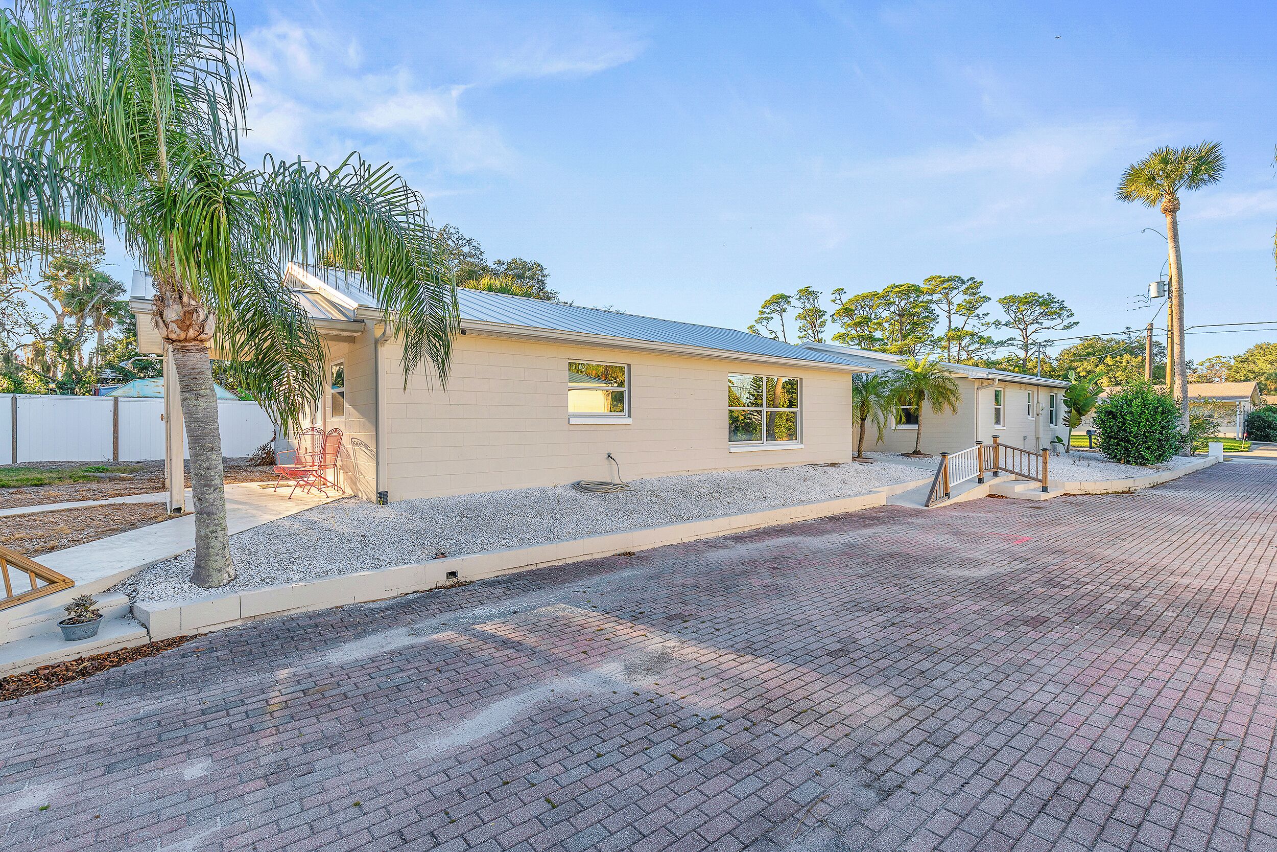 A single-story building with a flat roof, a paved driveway, and a small patio area with a chair and table.