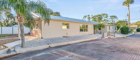 A single-story building with a flat roof, a paved driveway, and a small patio area with a chair and table.