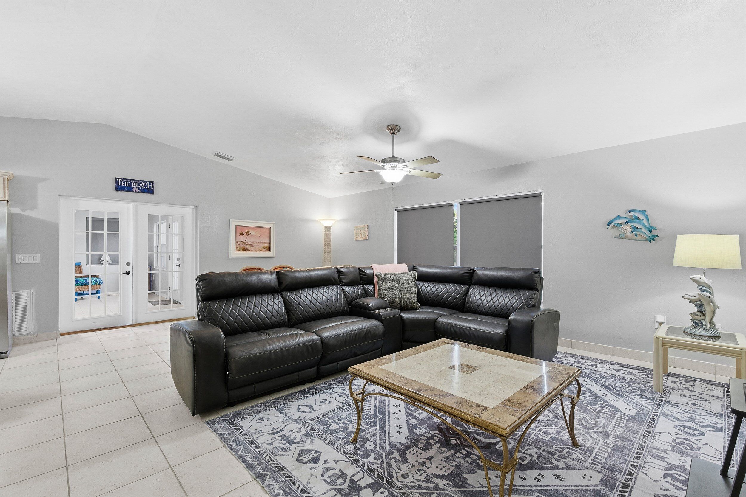 A living room with a black leather sectional sofa, a glass coffee table, and patterned rugs.