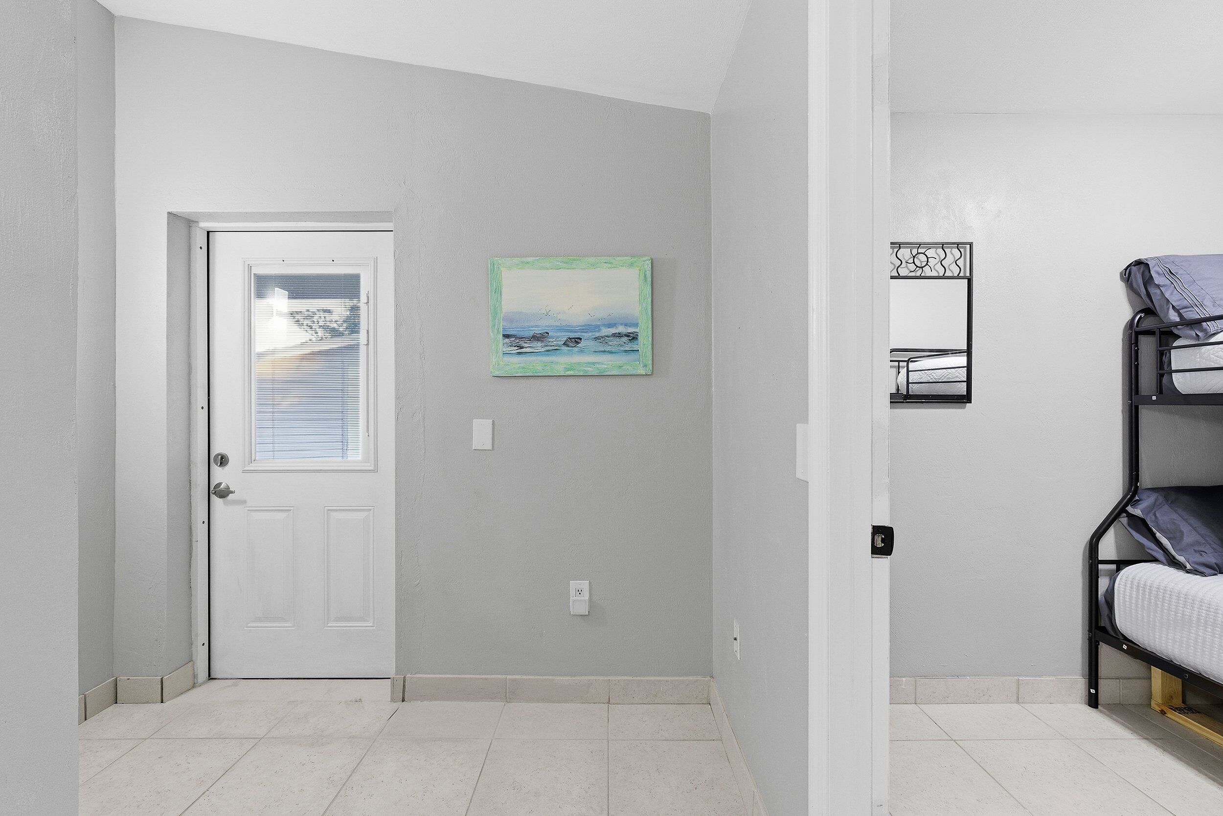 A room with a white door, a framed painting, a bunk bed, and a small mirror on the wall.