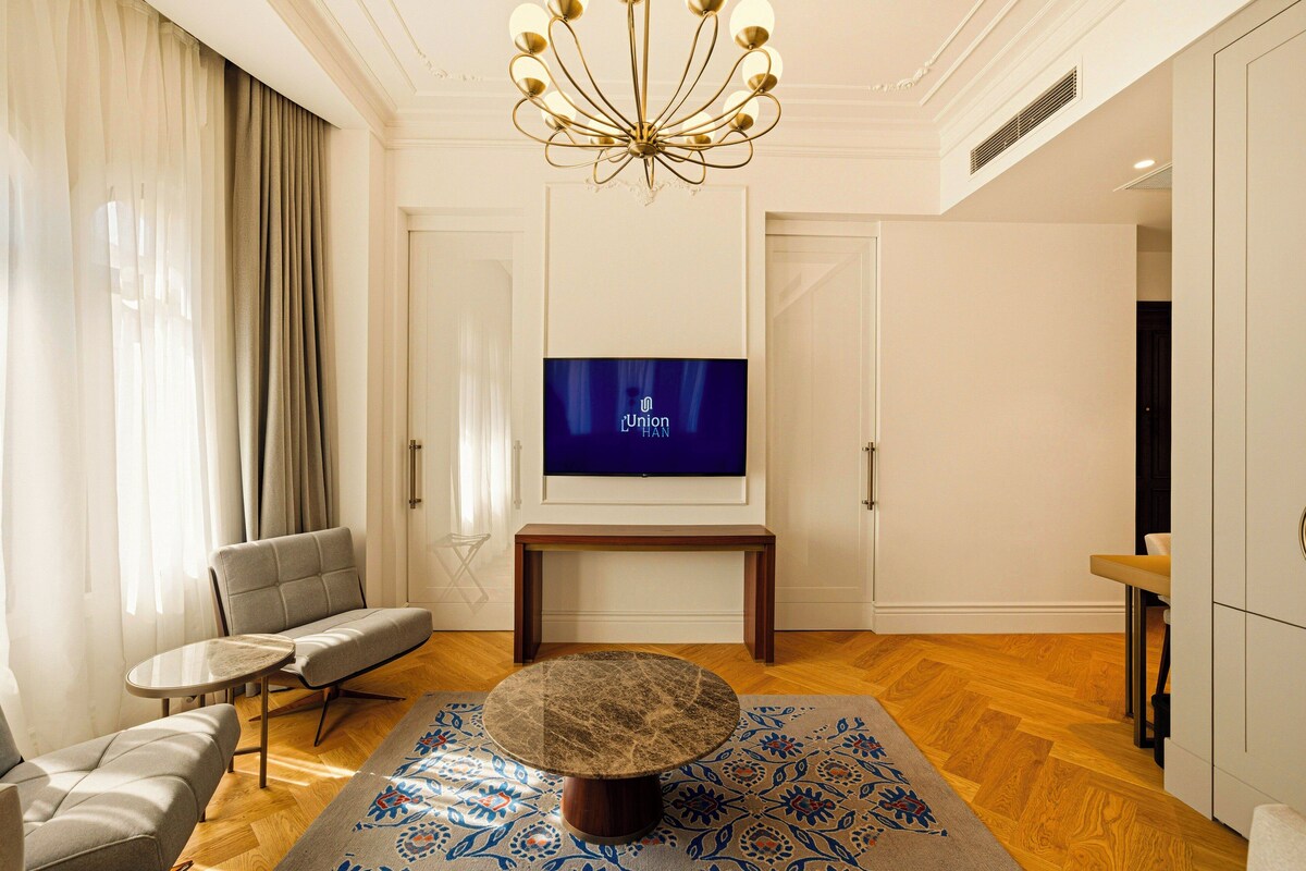 A modern living room with a sofa, a round coffee table, a television on a stand, and a patterned rug.