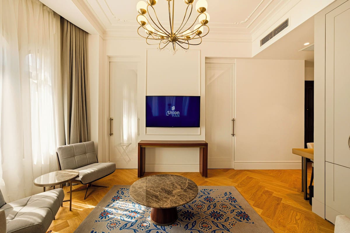 A modern living room with a sofa, a round coffee table, a television on a stand, and a patterned rug.