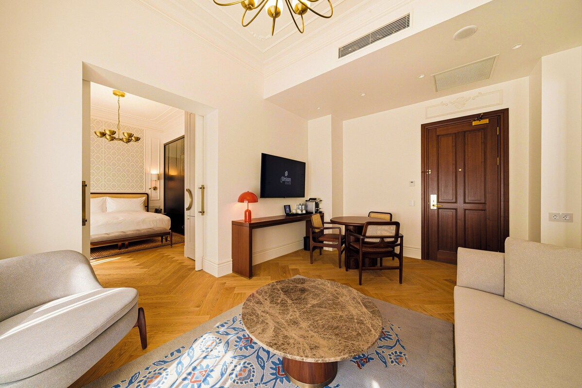 A hotel room with a bed, a desk, a television, a dining table with chairs, and a sofa.