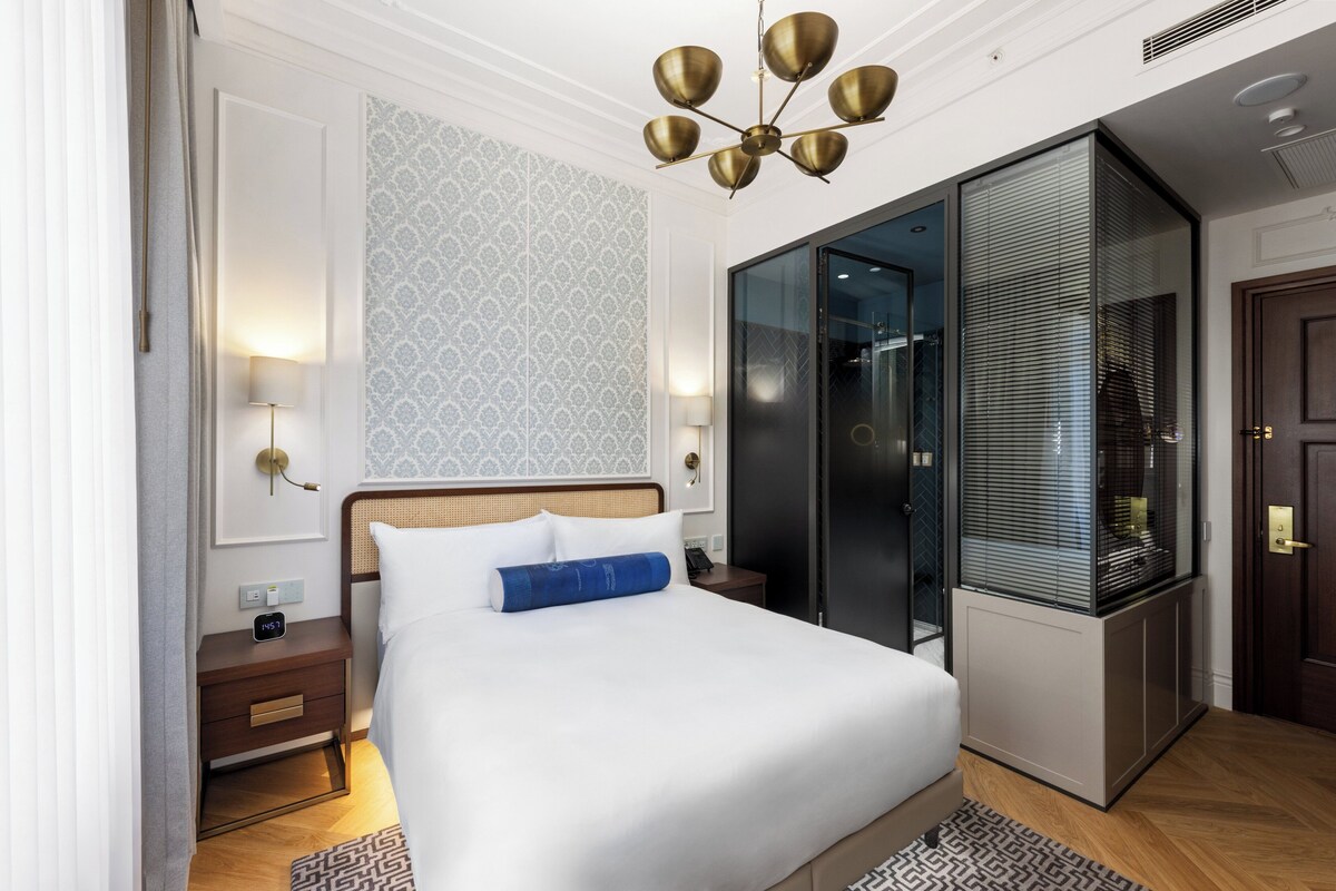 A modern hotel room with a large bed, bedside tables, a built-in wardrobe, and a glass shower enclosure.